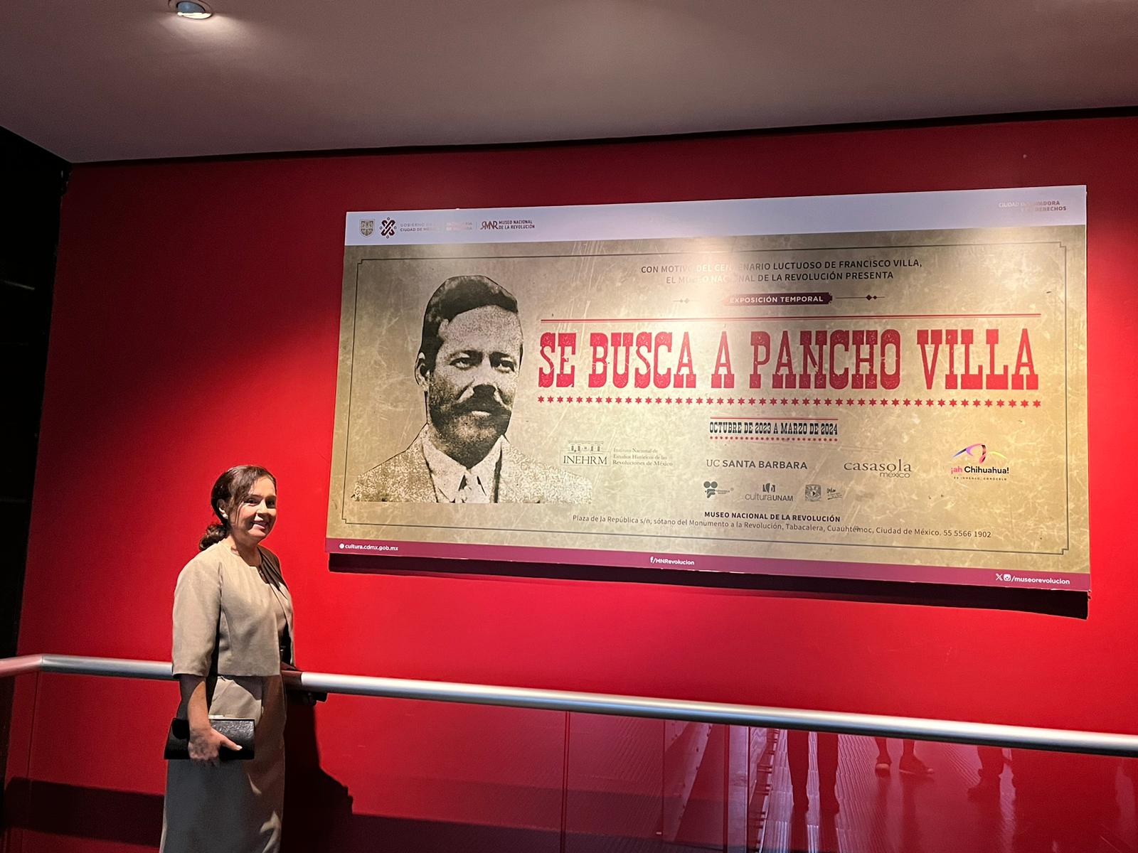 woman in front of large banner "Se Busca A Pancho Villa"