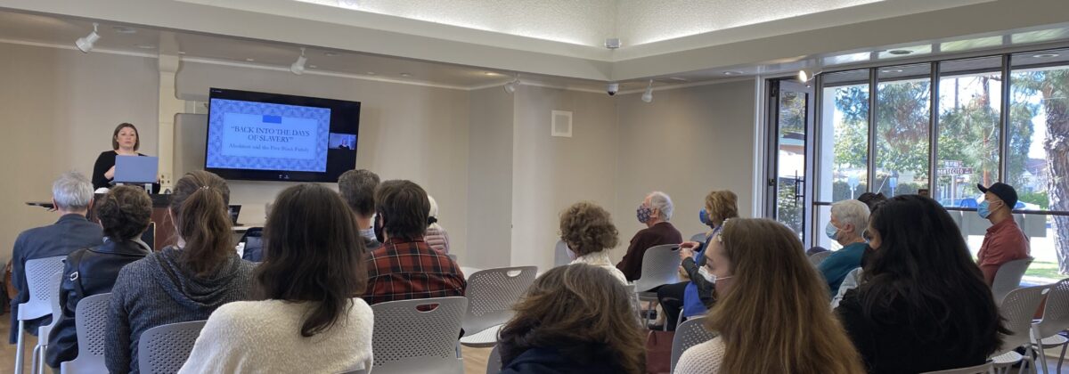 a room of people watch as a woman in a black shirt presents