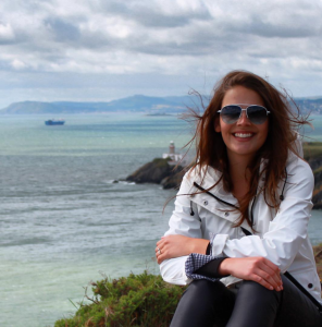 Caitlin Koford sitting on a cliff near the ocean and the end of a landmass with another landmass in the distance