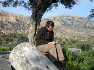 John W.I. Lee sitting on a rock with tree and mountains