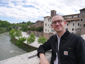 Doug Genens picture on a bridge over water with buildings in the background