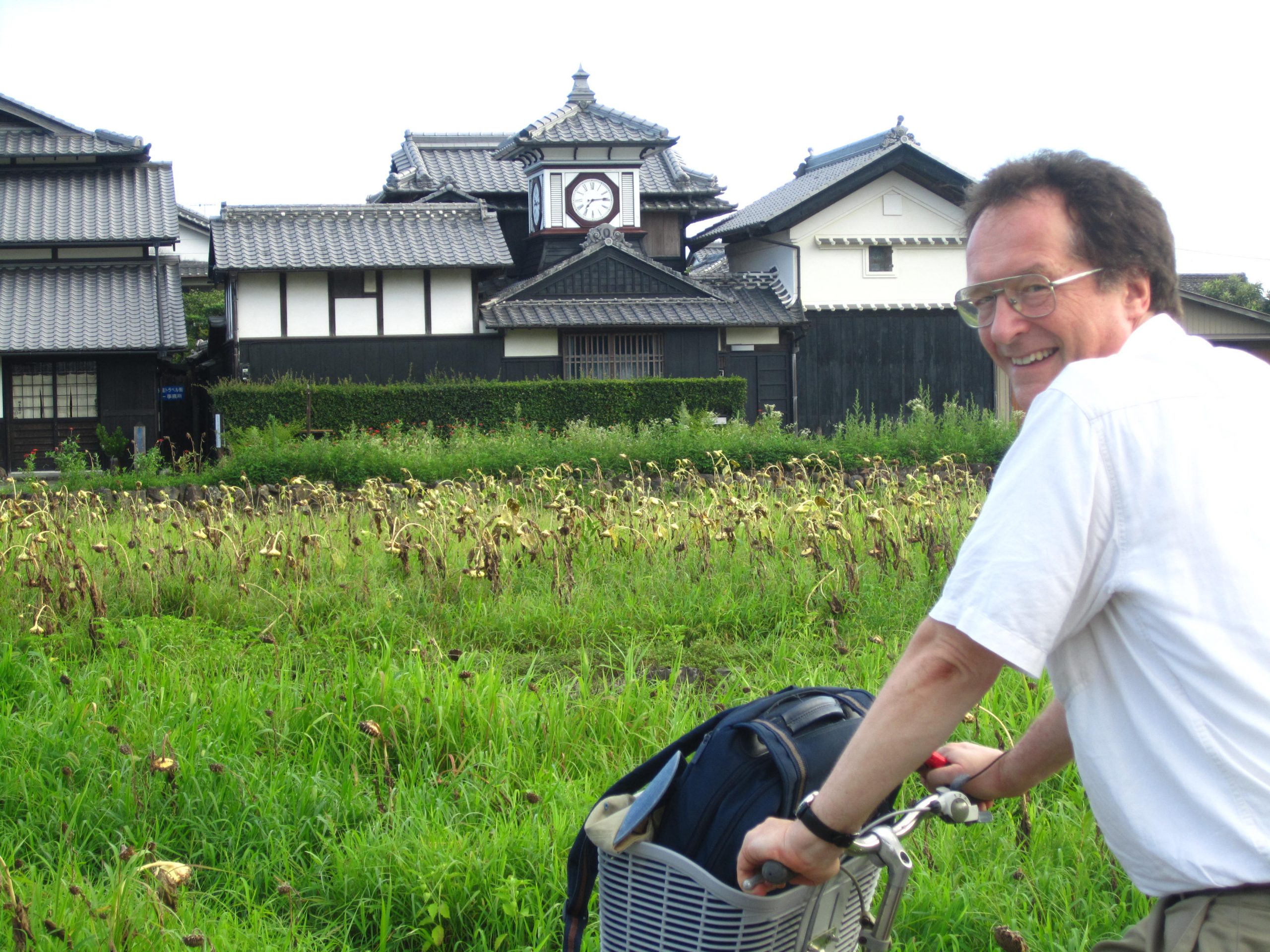 Luke Roberts on a bicycle in front of a field and a building