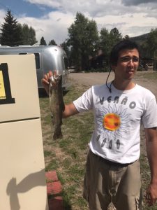 Andrew Elrod posing with a fish at a camp ground with campers in the background